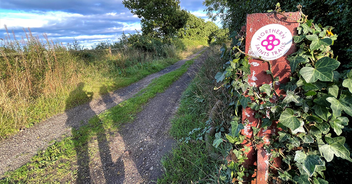 Shadow of people walking next to Northern Saints Trails waymarker